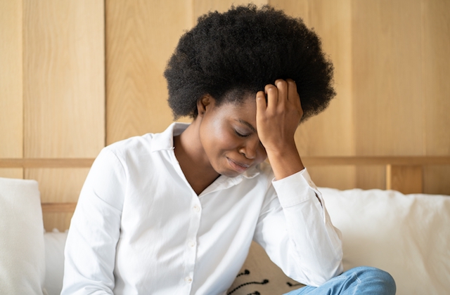 Black woman with an afro faces down with hand on forehead, looking depressed.