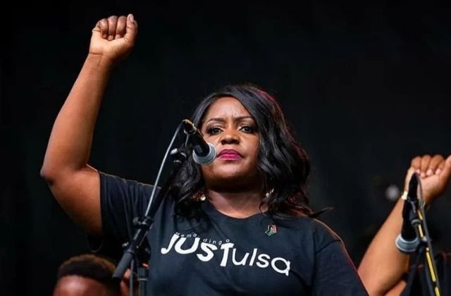 Tiffany Crutcher, founder of the Terence Crutcher Foundation, with her fist in the air. She wears a black t-shirt that reads: Just Tulsa. 