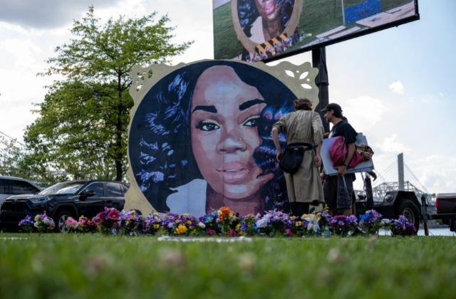 A painted mural of Breonna Taylor surrounded by flowers on a grassy lawn.