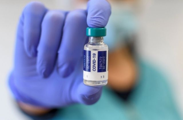 Close-up selective focus image of medical worker with blue gloves holding covid vaccine vial.