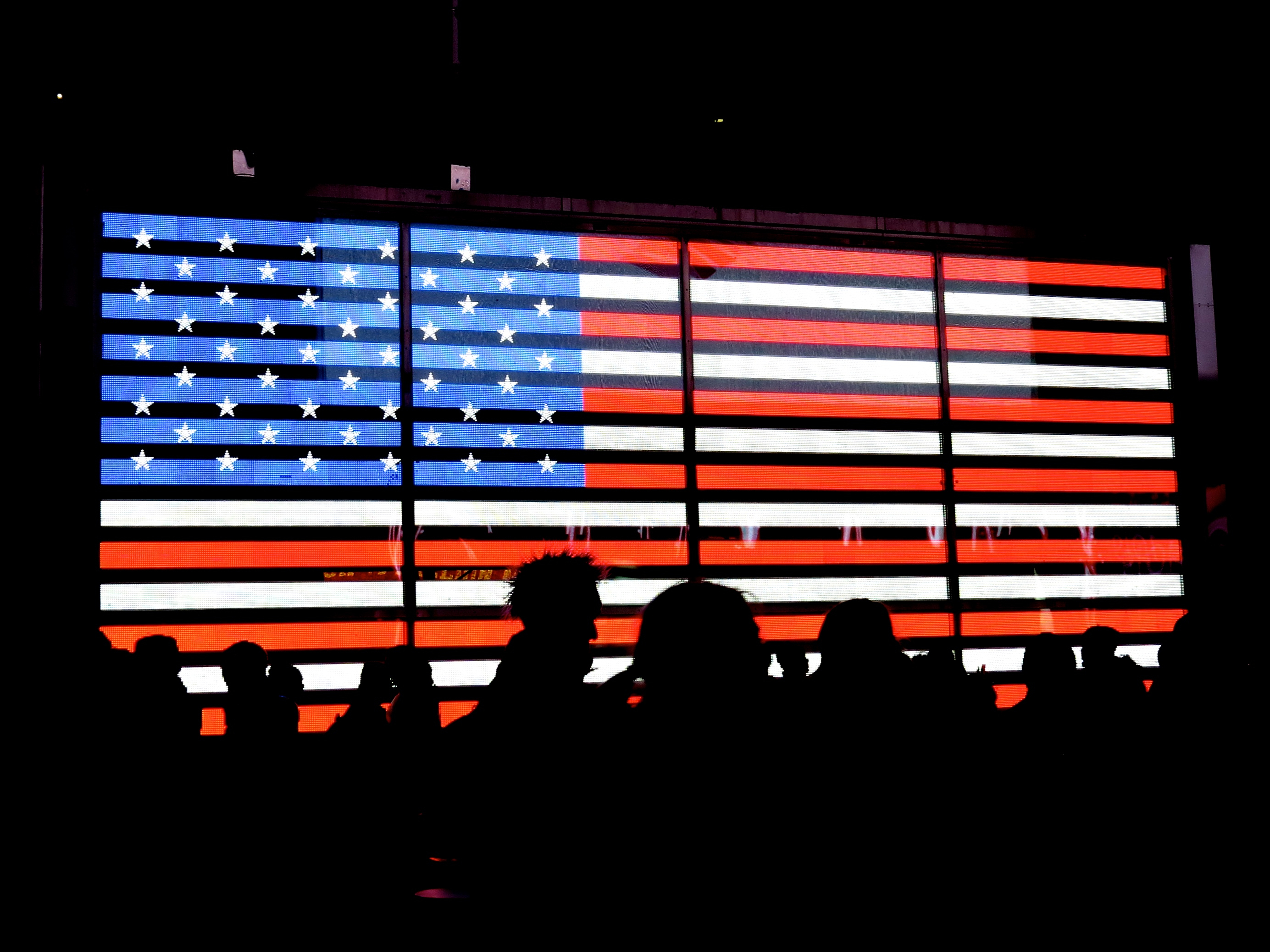 An image of the American flag with the silhouettes of people standing in front of it