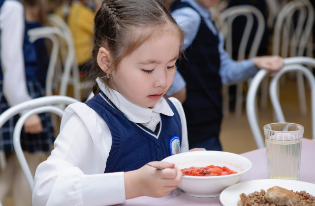 A young girl in a school uniform, eats lunch