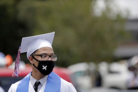 A student in a graduation cap and gown dons a mask with their stole during the COVID-19 pandemic.