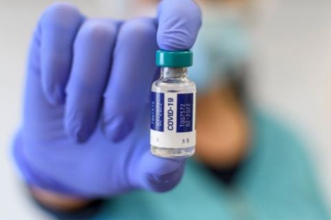 Close-up selective focus image of medical worker with blue gloves holding covid vaccine vial.