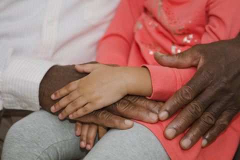 A close-up photo of hands as a Black child sits on their grandparent's lap.